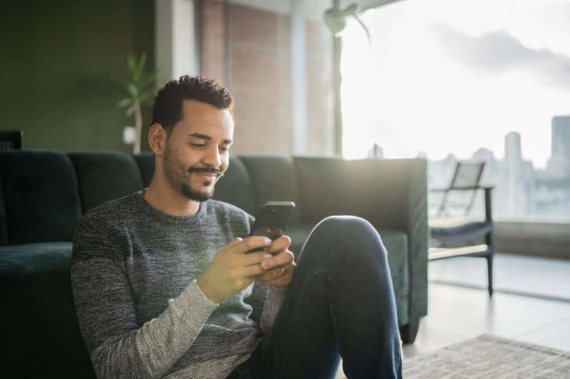 Man sitting in living room using is smartphone to order cannabis online in pahrump with the skyline in background